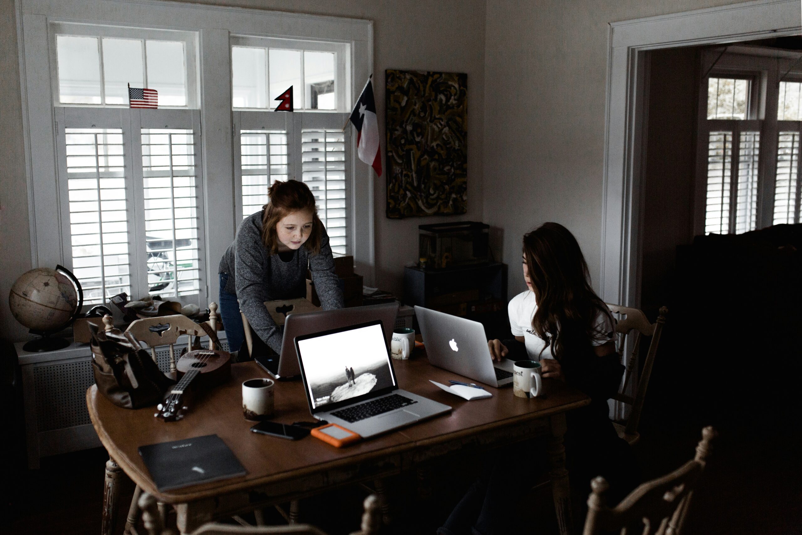 Two ambitious women sit at a table with in a moody workspace with their laptops open, hunting for their best work receipts