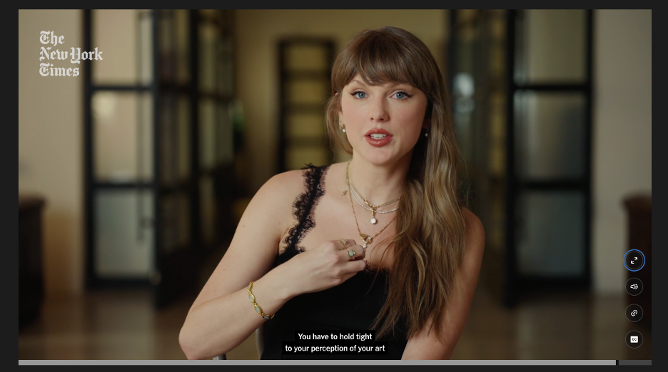 Screen cap of Taylor Swift in conversation with The New York Times on April 28, 2026. Closed captioning reads: 'You have to hold tight to your perception of your art.' Swift speaks directly to camera with one hand touching her torso. She's wearing a black tank top with lacy straps, multiple thin necklaces, a bracelet, earrings and several rings. Her long hair is down and pulled to her left shoulder.